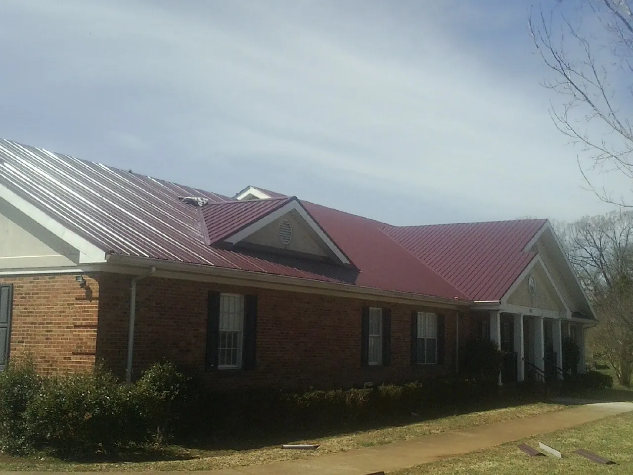 Red metal roof with gabled entries on a long brick building, from a Hail Damage Roof Repair job in Caneyville
