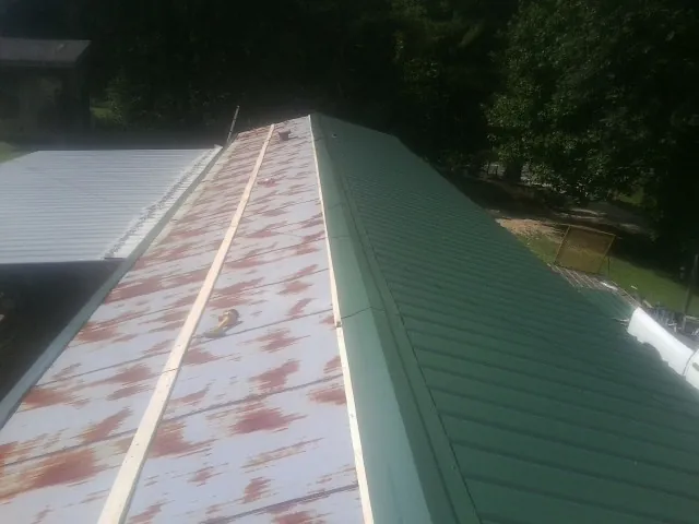 Old rusted panels beside newly installed green metal roofing — Wind Damage Roof Repair by Roofing Brothers in Caneyville