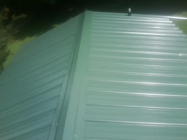 New green metal panels meeting at the ridge of a roof — Flat Roof Repair work by our crew in Caneyville