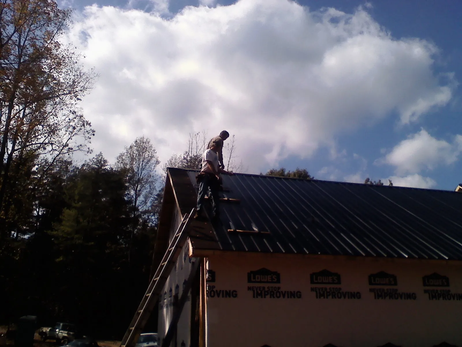 Roofer fastening dark metal panels high against a cloudy sky, from a Roof Inspection job in Caneyville