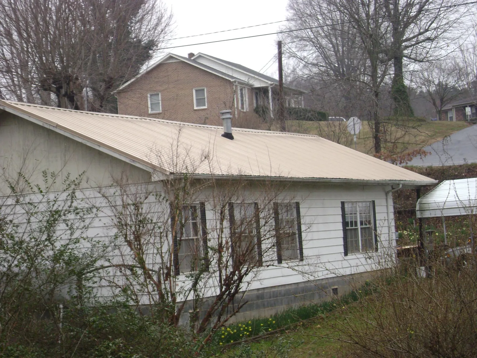 Tan metal roof on a white sided house set into a hillside — Commercial Roofing by Roofing Brothers in Caneyville