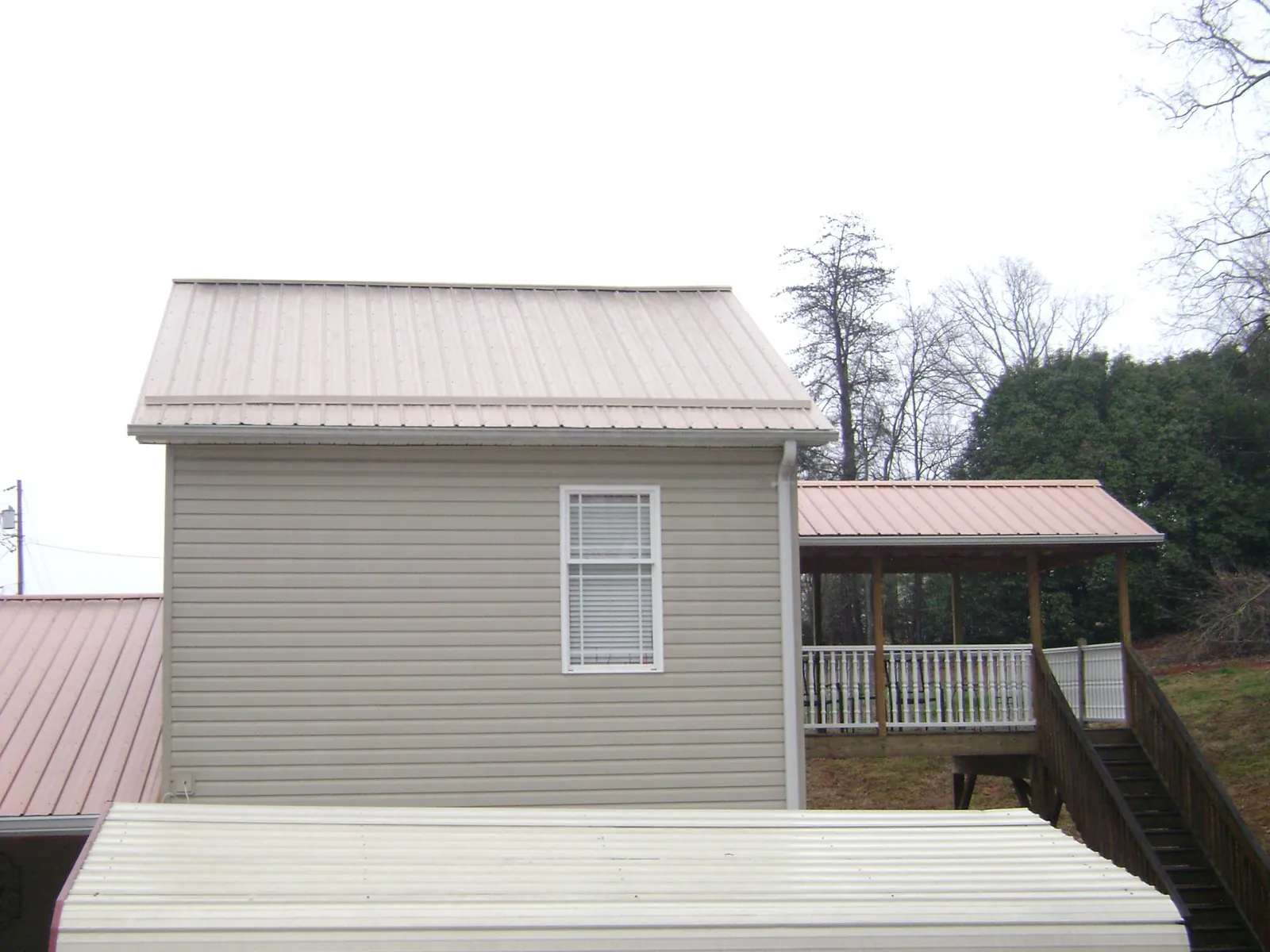 Tan metal roofs on a two story addition and attached porch, from a Roof Replacement job in Caneyville